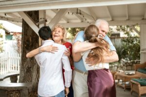 Elderly parents hugging their adult son and daughter, symbolizing how our financial habits often mirror our parents’ as we get older.