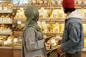 Two people standing in a grocery store bakery aisle, looking at shelves of bread and pastries.