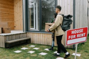 Young adult walking past a modern house with a “For Rent” sign, representing the challenges of homeownership for millennials and Gen Z.