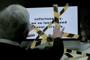 Employee standing in front of a screen with a layoff notice blocked by caution tape.