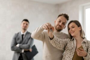 A couple holding a house key while a real estate agent stands behind them during a home purchase.