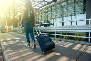 Traveler walking through an airport terminal with a rolling suitcase, sunlight coming through the glass structure.